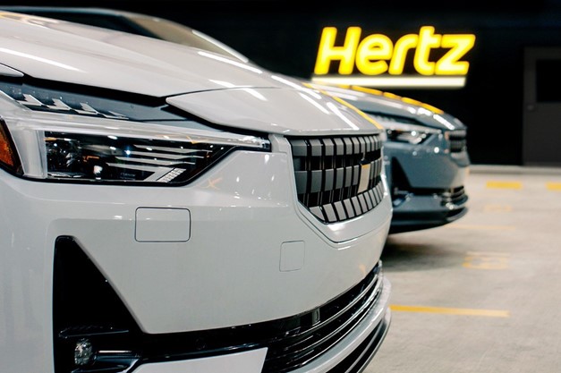 A Polestar 2 pictured in a rental lot with the Hertz logo glowing in the background.