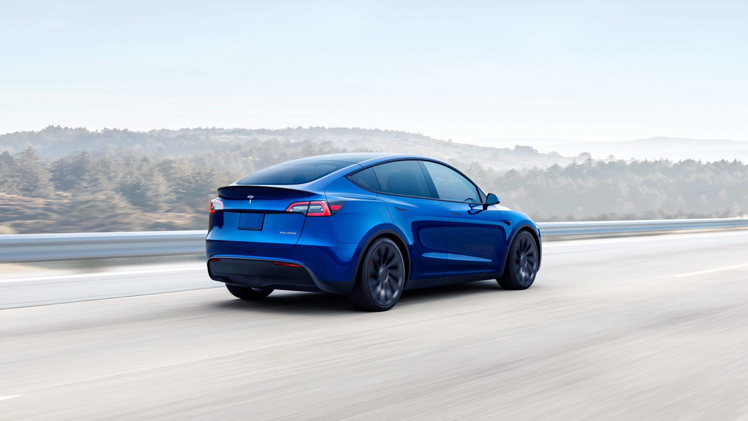 A blue Tesla Model Y driving down a scenic parkway.
