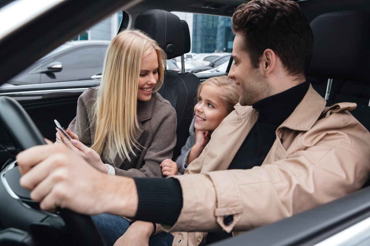 Family sitting inside a car and smiling together during a drive, representing a quieter and more comfortable cabin experience with automotive sound deadening materia